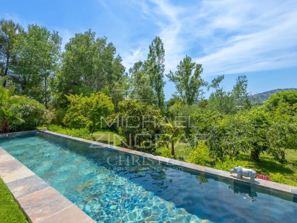 Vue de la piscine et du jardin d'une villa moderne à Grasse, avec des arbres et la campagne en arrière-plan.