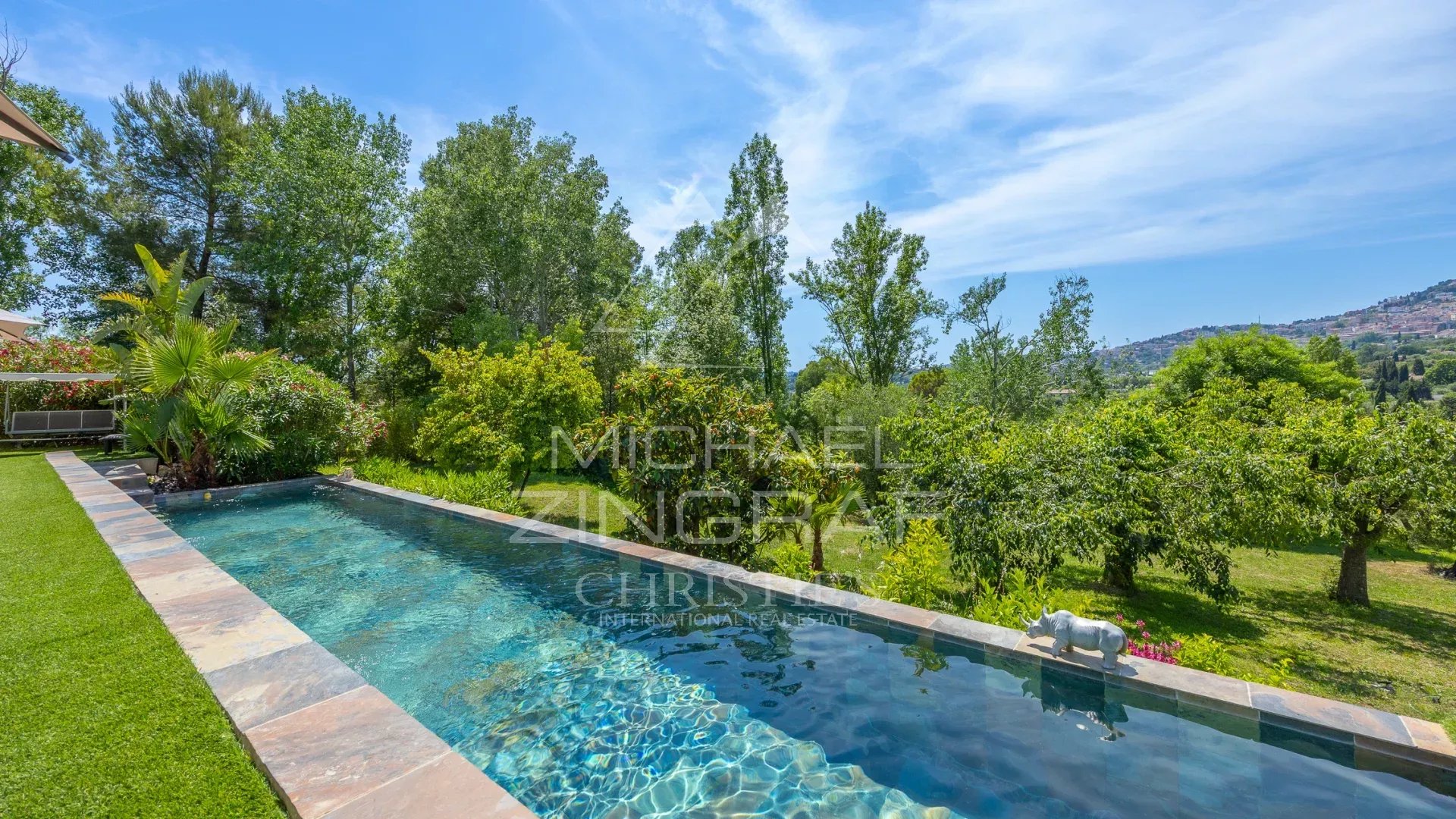 Villa moderne avec piscine à Grasse Vue de la piscine et du jardin d'une villa moderne à Grasse, avec des arbres et la campagne en arrière-plan.