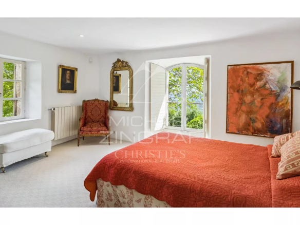 Chambre d'une propriété en pierre avec vue sur la nature, décorée avec un tableau et un fauteuil ancien.