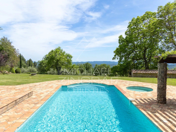 Vue d'une piscine avec un espace extérieur verdoyant et des collines en arrière-plan.