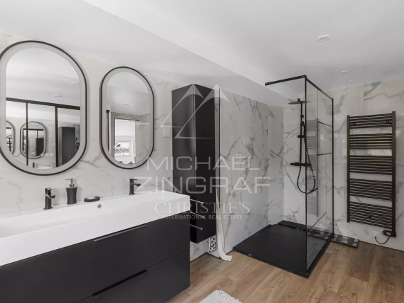 Modern bathroom with double white sinks, black fixtures, and rounded mirrors over marble walls.