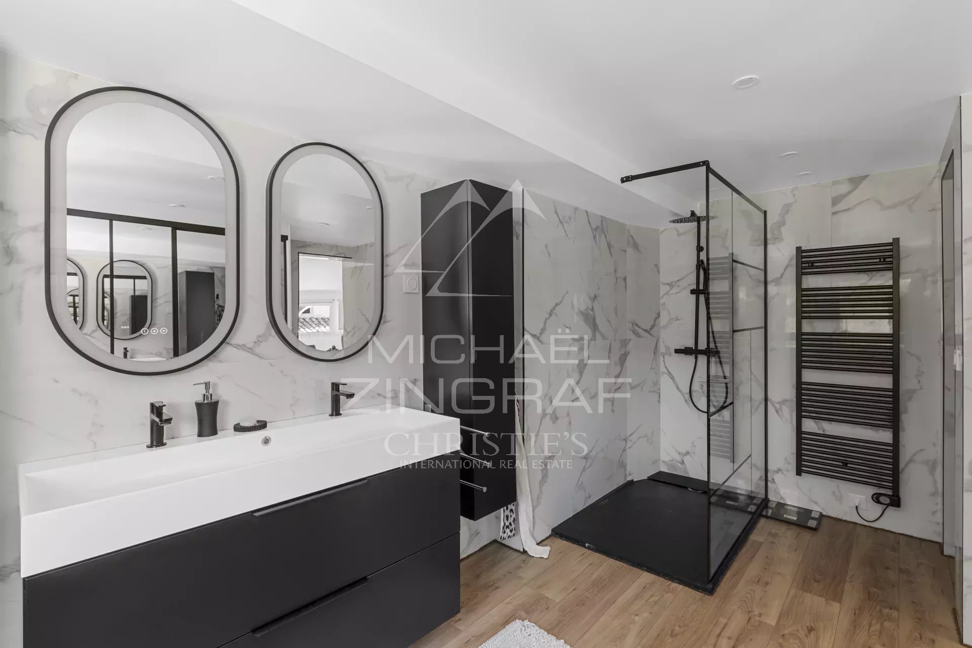 Modern bathroom with double white sinks, black fixtures, and rounded mirrors over marble walls.