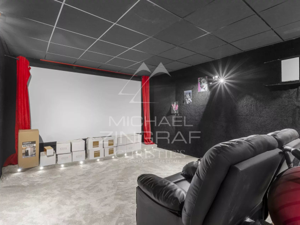 Home cinema room with a large white projection screen, red curtains, and a black-wall background; boxes line the baseboard and a plush recliner is in the foreground.