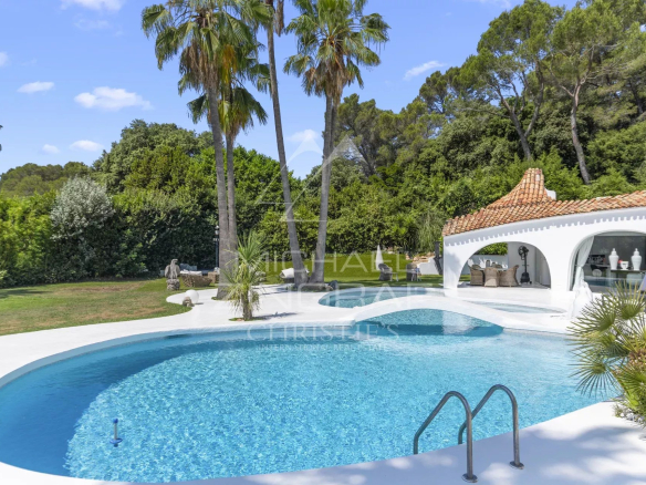 Outdoor pool with a curved blue-tiled edge, white deck, and palm trees in a sunny garden setting