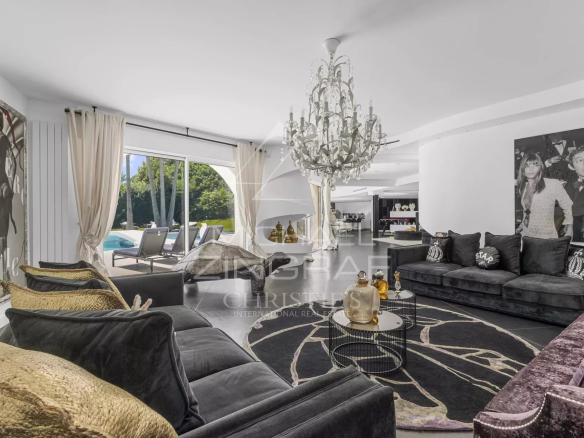 Luxurious black-sofa living room with a crystal chandelier, large curtains, and a view of the outdoor pool area through sliding doors.