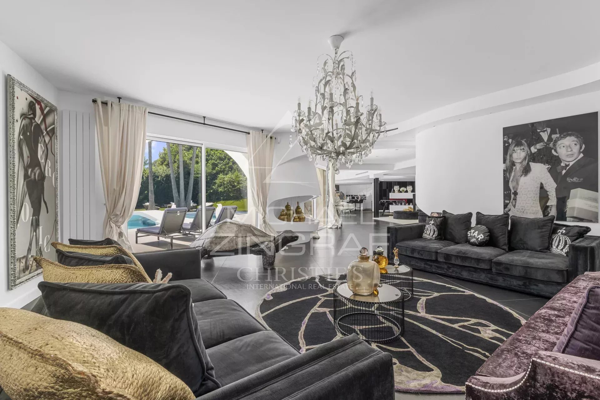 Luxurious black-sofa living room with a crystal chandelier, large curtains, and a view of the outdoor pool area through sliding doors.