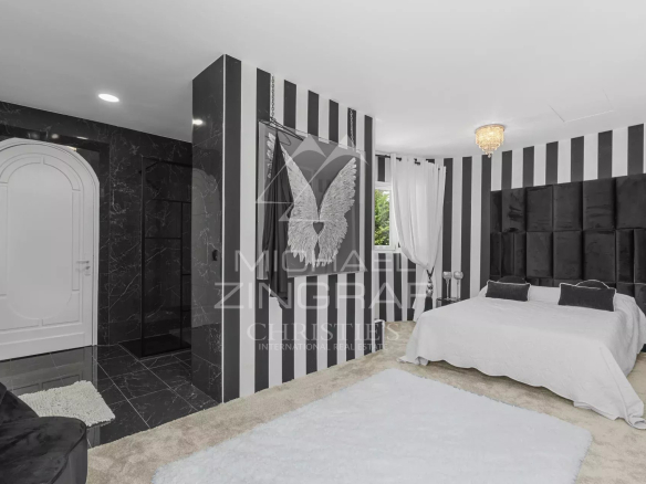 Luxurious bedroom with black-and-white vertical stripes, a large bed with a tufted dark headboard, white linens, and a chandelier.
