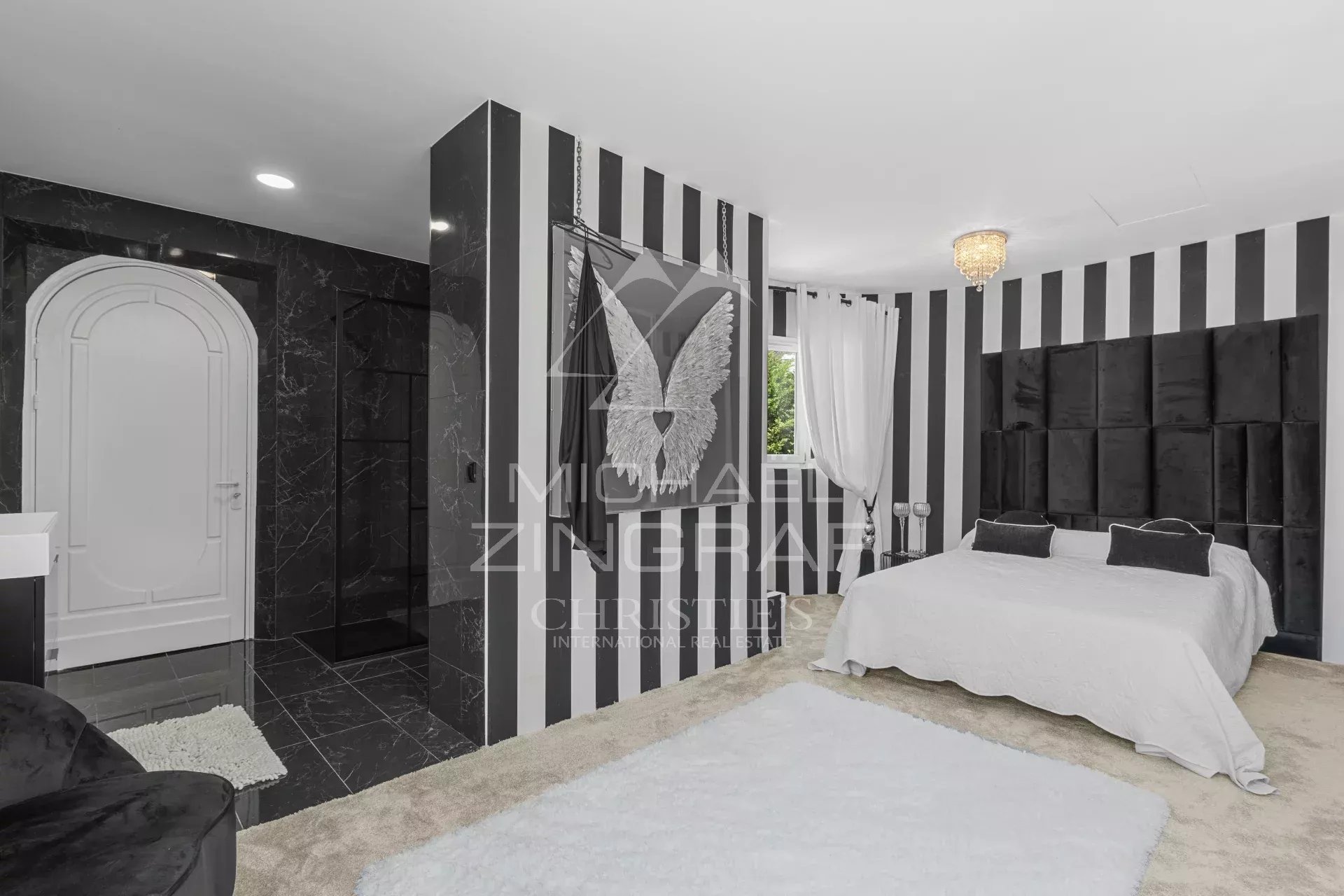 Luxurious bedroom with black-and-white vertical stripes, a large bed with a tufted dark headboard, white linens, and a chandelier.