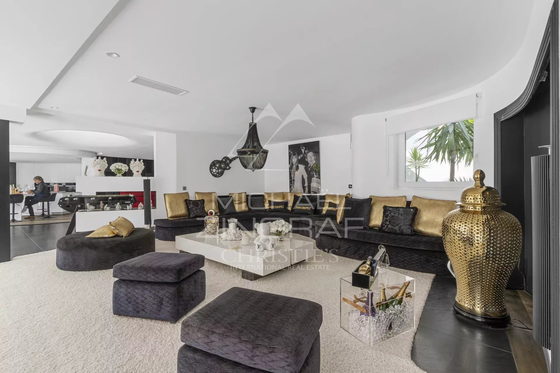 Luxurious open-plan living room with black and gold sectional seating, white rug, and decorative gold vase centerpiece.