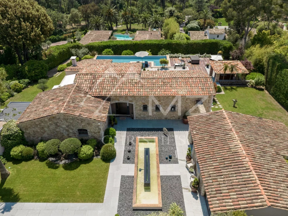 Aerial view of a stone villa with terracotta roofs, central courtyard, and a long rectangular water feature surrounded by gravel and greenery at the front.