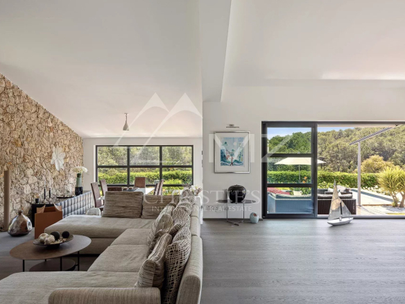Bright open-plan living room with a stone feature wall, neutral sofa, and a views of the outdoor pool through large glass doors.