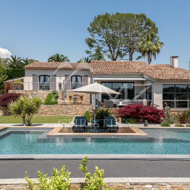 Luxurious single-story villa with a terracotta roof, glass walls, and an inviting in-ground pool surrounded by a stone terrace and garden beds.