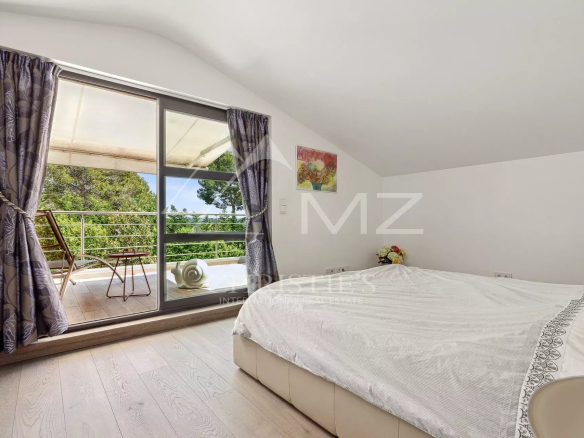 Bedroom with a large glass door to a balcony, purple patterned curtains, white bed, and wooden floor.