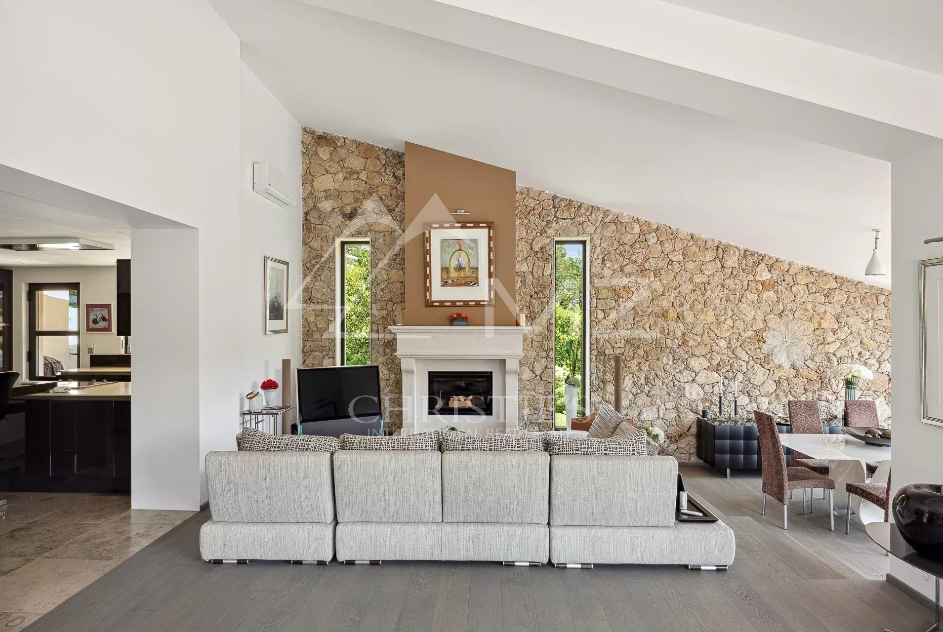 Open-plan living room with a stone feature wall, white fireplace, and a large gray sectional sofa facing a TV.