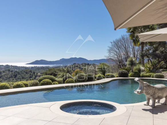 Luxurious pool terrace with a circular hot tub, beige tiles, and a coastal valley view; a hippo statue by the pool.