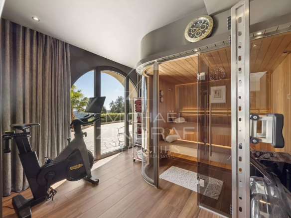 Stationary bike in a bright wellness room beside a glass-front wooden sauna.