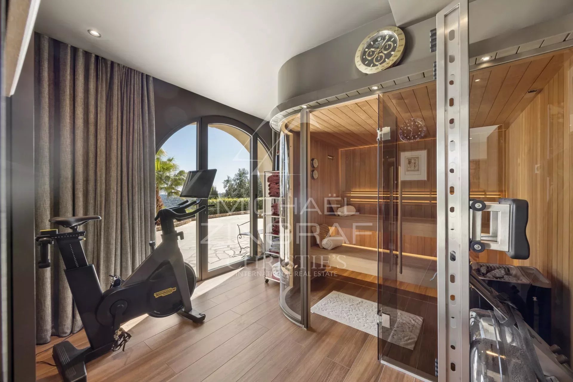 Stationary bike in a bright wellness room beside a glass-front wooden sauna.