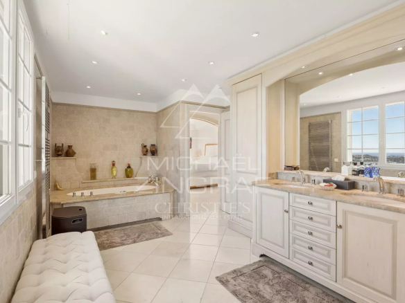 Luxurious beige bathroom with a built‑in tub, double-sink vanity, and large windows with a city view.