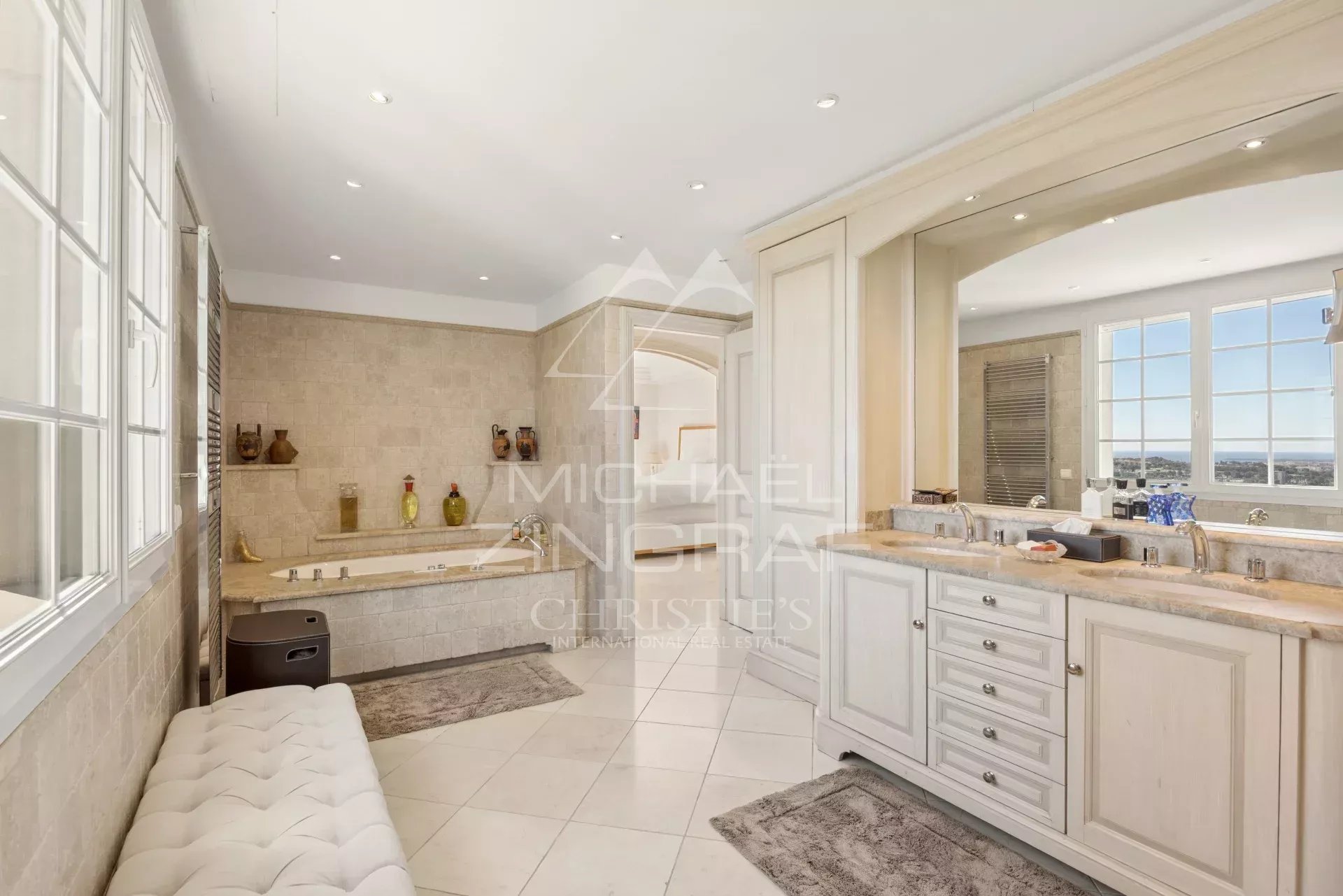 Luxurious beige bathroom with a built‑in tub, double-sink vanity, and large windows with a city view.