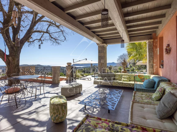 Outdoor covered patio with colorful cushioned seating, metal table, and view of hills and blue sky.