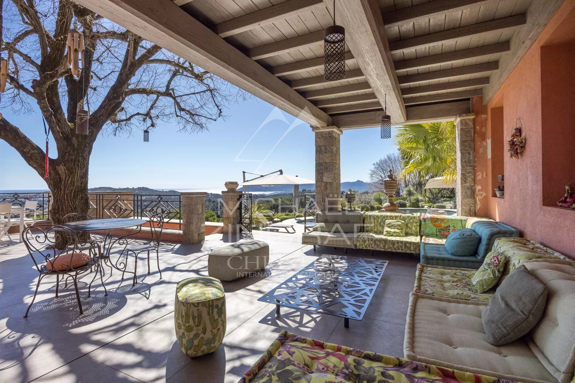 Outdoor covered patio with colorful cushioned seating, metal table, and view of hills and blue sky.