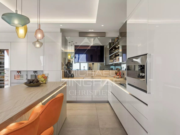 Modern white kitchen with a marble island, orange bar stools, and pendant lights hanging above the island.