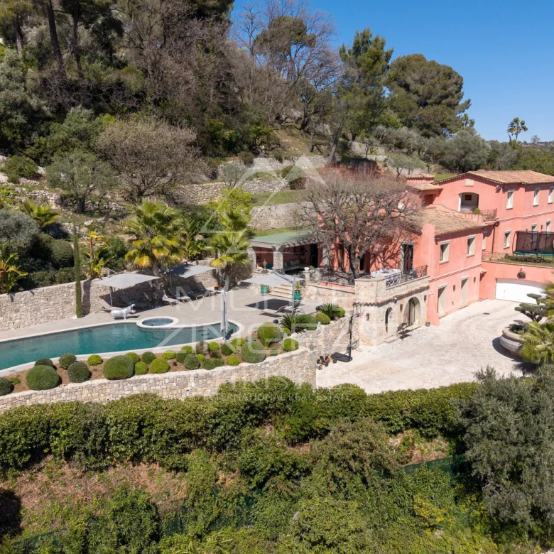 A pink hillside villa with a curving pool, stone patio, and manicured shrubs overlooking terraced gardens.