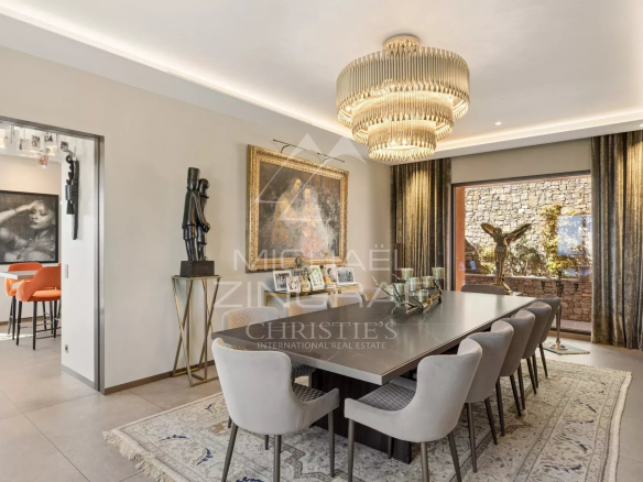 Luxurious dining room with a long glass-top table, upholstered chairs, and a tiered chandelier centerpiece.