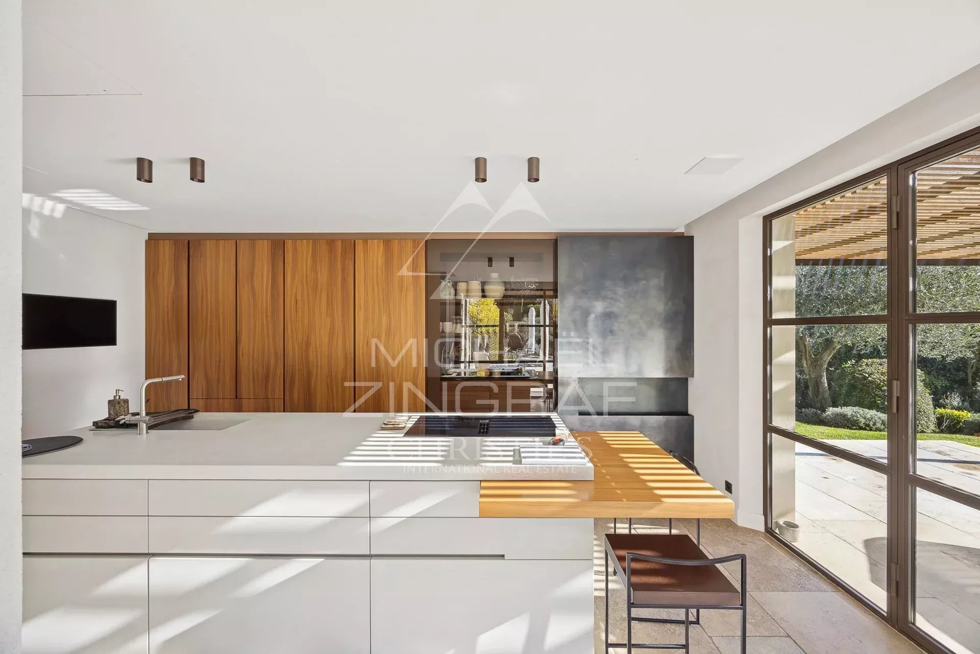 Modern kitchen with a white island, warm wood cabinets, and large glass doors opening to a garden.