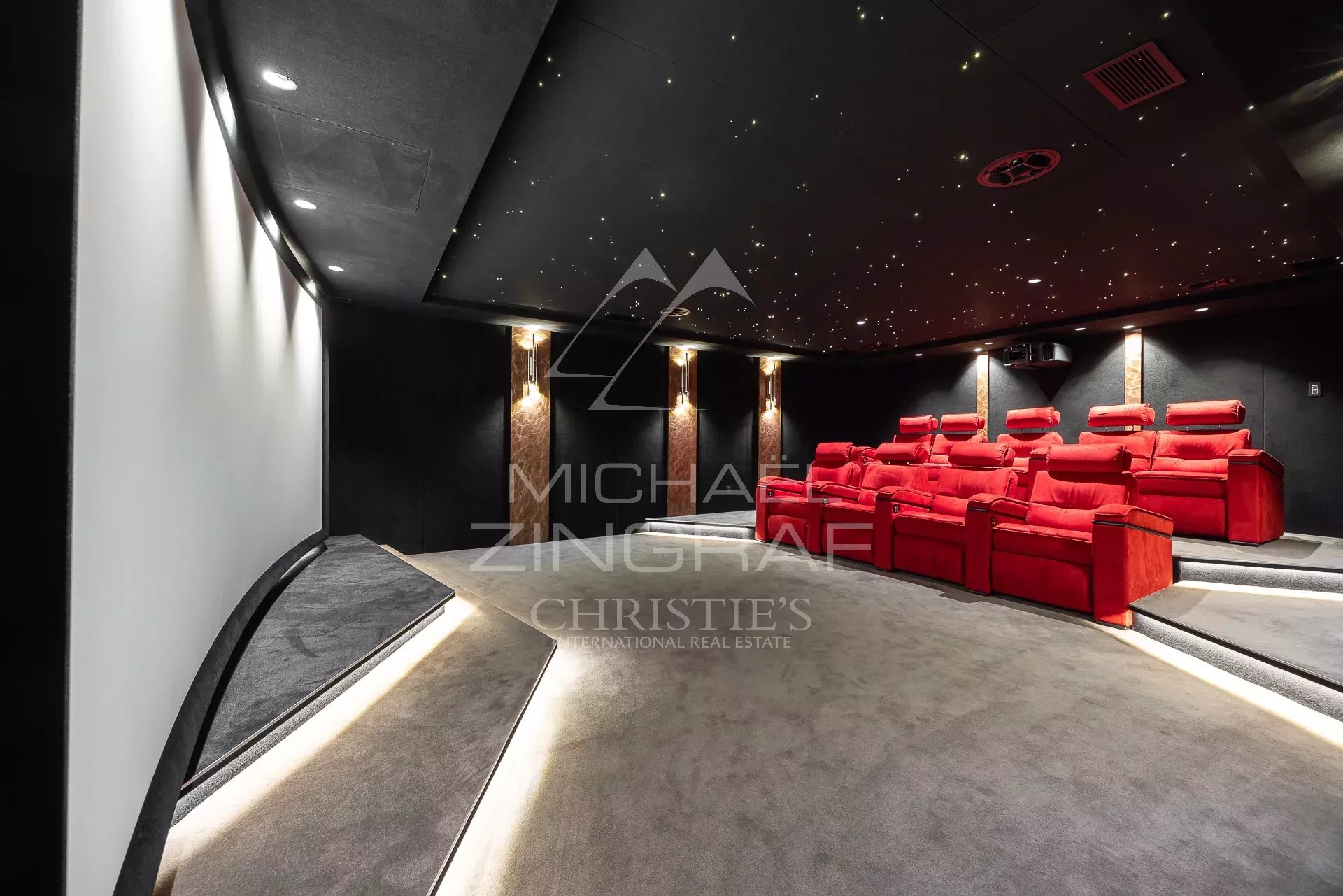 Private home theater with red plush recliner seats in tiered rows, dark walls, and a starry, illuminated ceiling.
