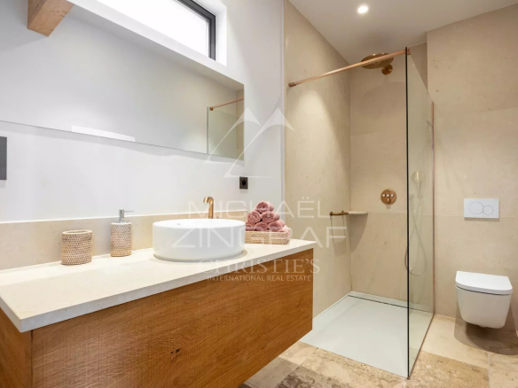 Contemporary bathroom featuring a wooden vanity with a round white basin and gold faucet, large mirror, and a glass-enclosed shower area.