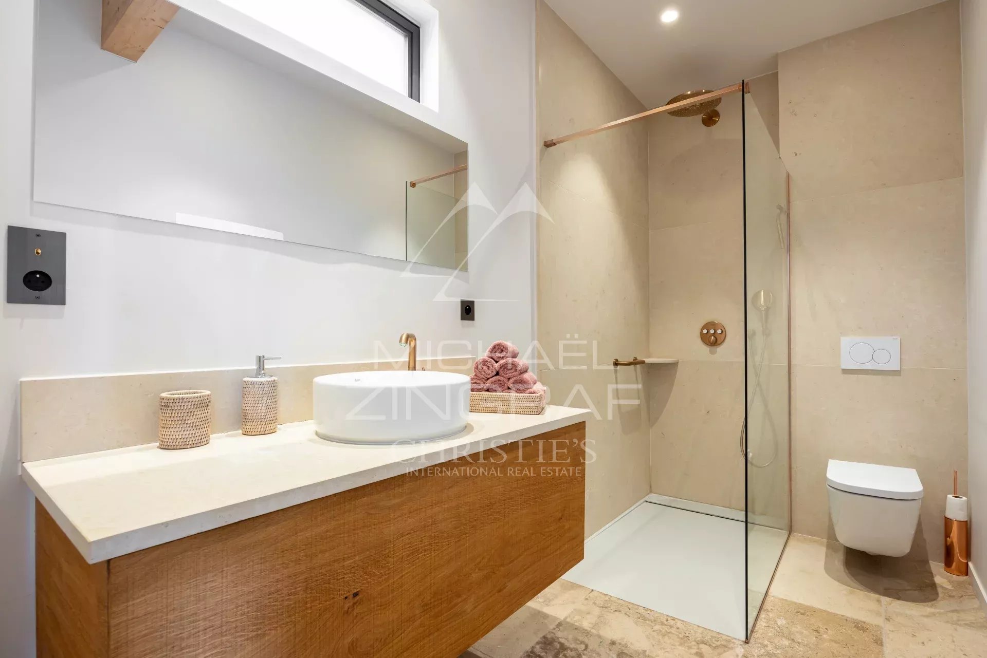 Contemporary bathroom featuring a wooden vanity with a round white basin and gold faucet, large mirror, and a glass-enclosed shower area.