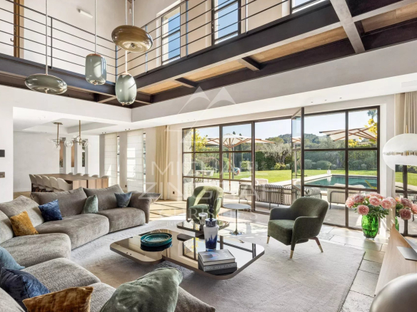 Spacious modern living room with gray sectional sofa, green chairs, and a glass coffee table, opening to a sunny patio and pool.