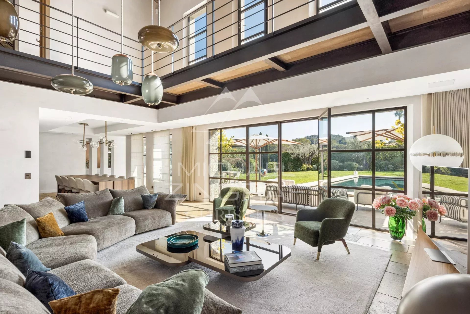 Spacious modern living room with gray sectional sofa, green chairs, and a glass coffee table, opening to a sunny patio and pool.