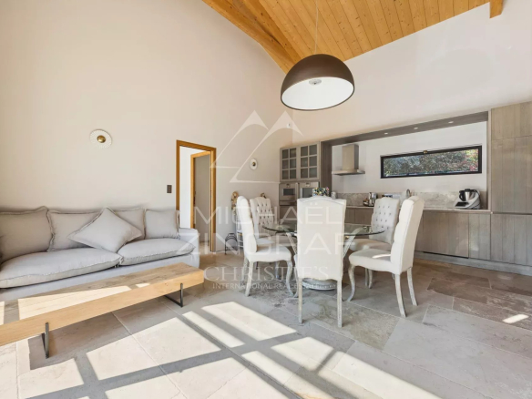 Open-plan living and dining area with light gray sofa, wooden coffee table, and white upholstered dining chairs facing a modern kitchen.