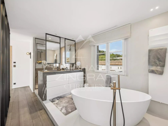 Contemporary bathroom with a freestanding white tub, marble-topped vanity, and a glass-framed partition by a large window.