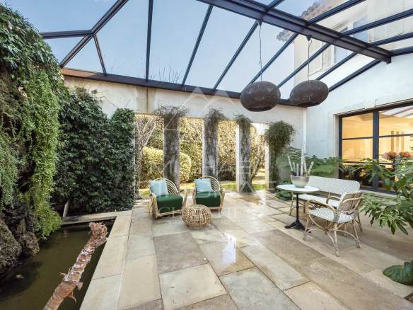 Glass-covered patio with wicker seating area and potted plants, overlooking a garden.