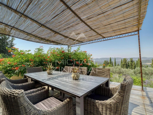 Terrasse d'une villa provençale avec mobilier en osier et vue sur les collines et la mer.