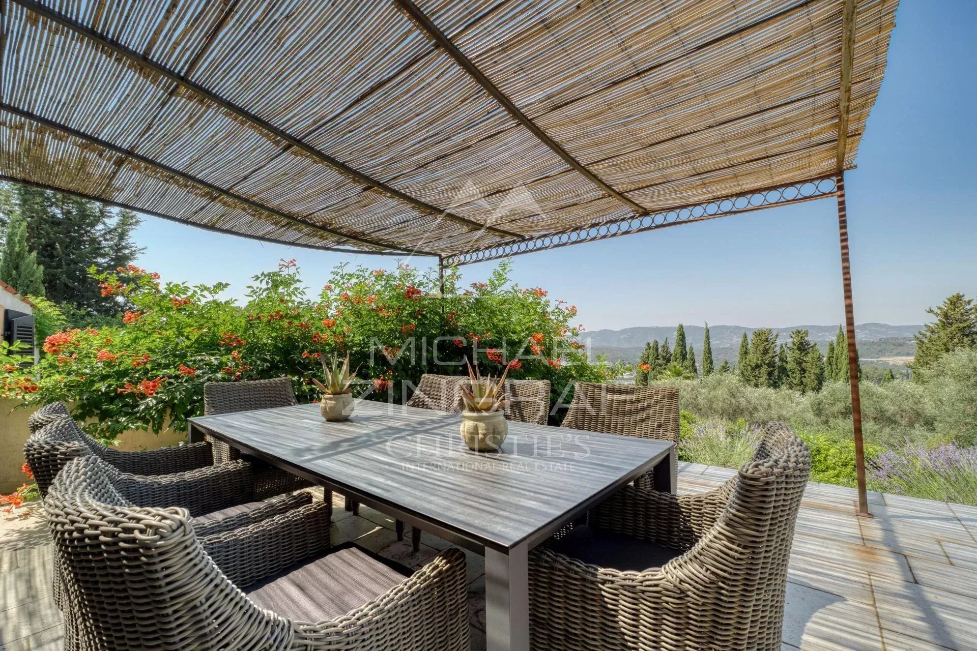 Terrasse d'une villa provençale avec mobilier en osier et vue sur les collines et la mer.