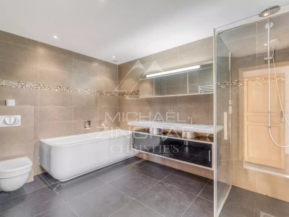Salle de bain moderne avec baignoire et douche, carrelage gris et éclairage LED.