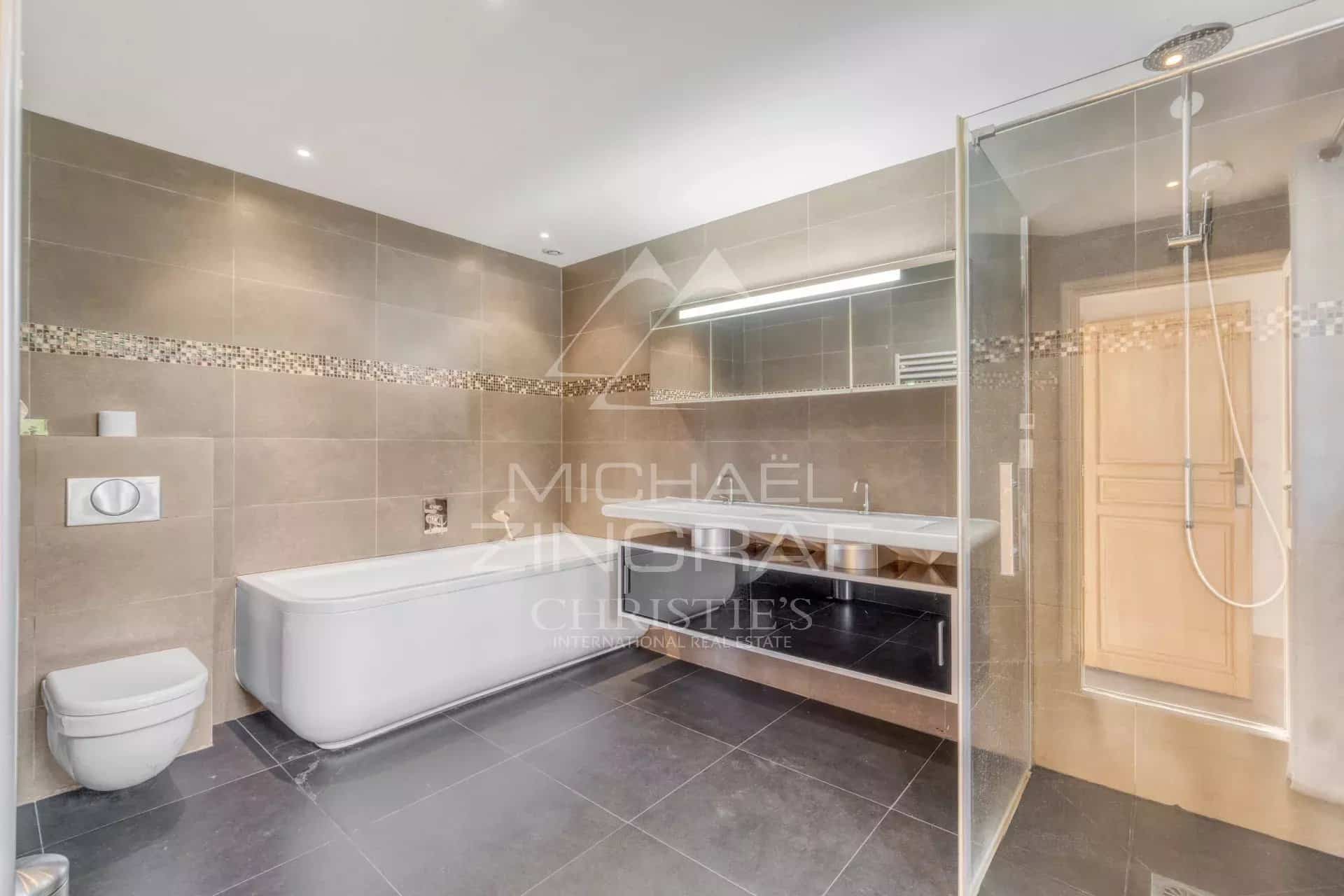 Salle de bain moderne avec baignoire et douche, carrelage gris et éclairage LED.
