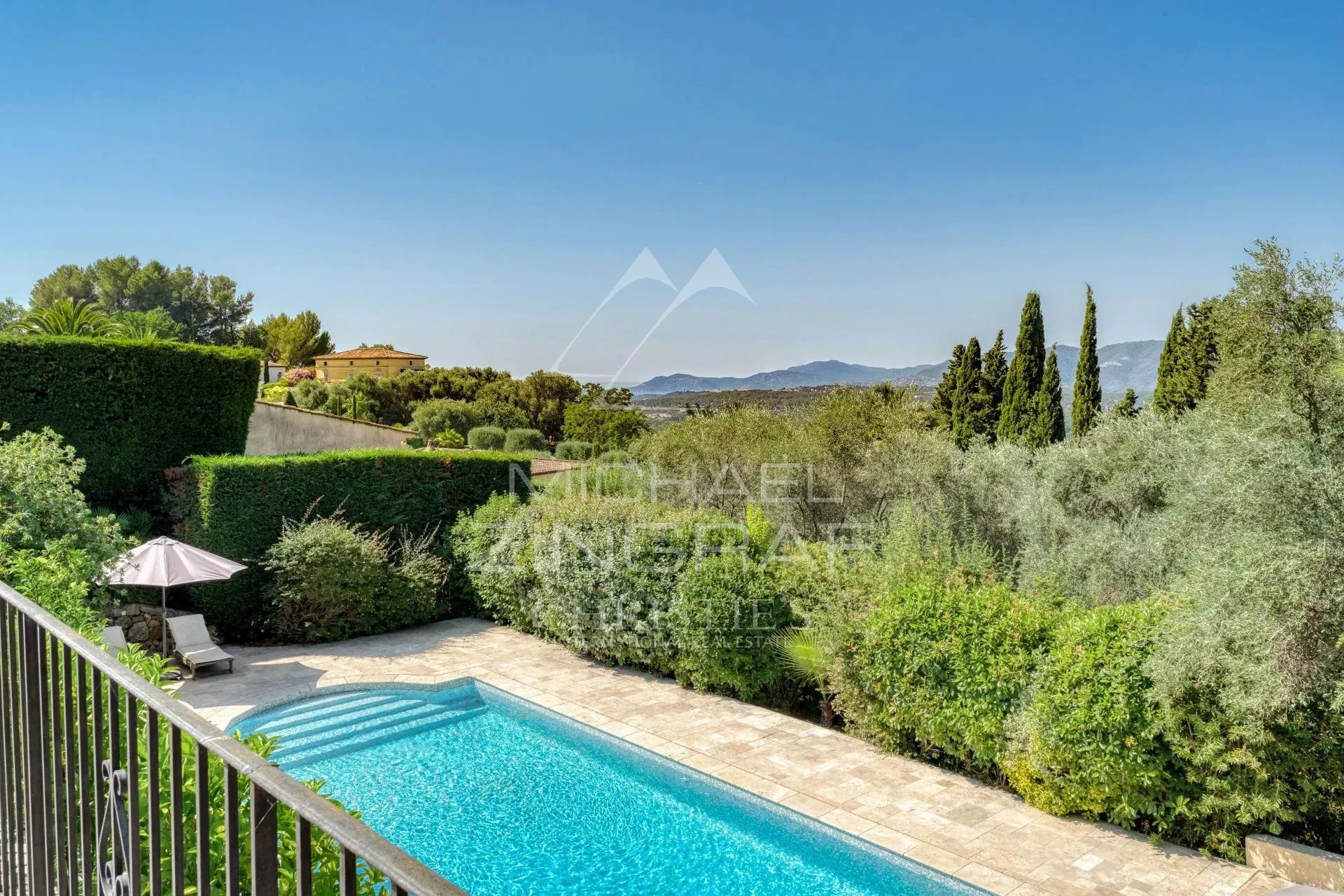 Vue d'une villa provençale avec piscine et jardin, entourée de collines et d'arbres.