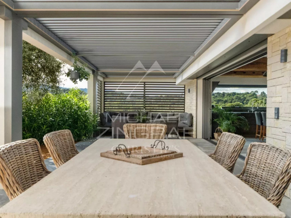 Terrasse d'une villa moderne avec table en pierre et chaises en osier, vue sur un environnement verdoyant.