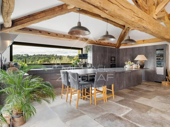 Intérieur d'une cuisine moderne avec poutres apparentes et vue sur la nature.