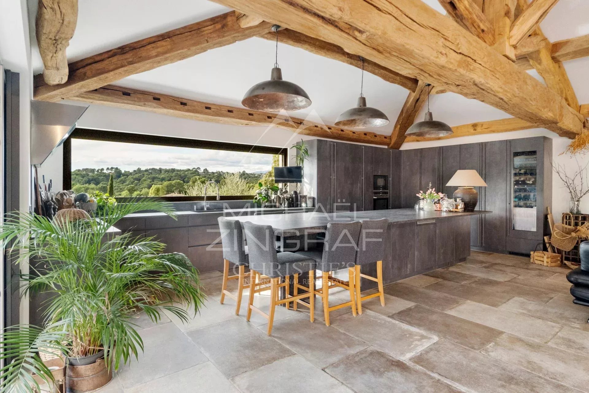 Intérieur d'une cuisine moderne avec poutres apparentes et vue sur la nature.