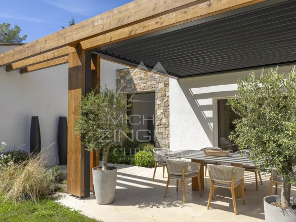Terrasse d'une villa provençale contemporaine avec table en bois et chaises, entourée de verdure.