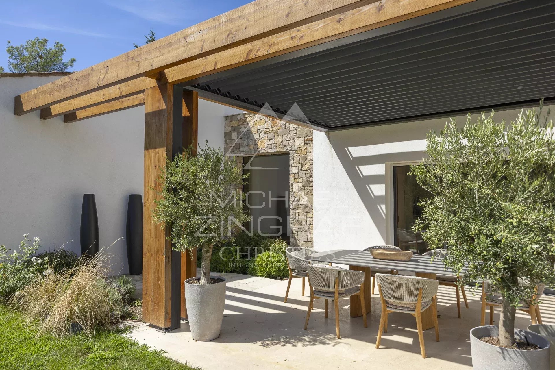 Terrasse d’une villa à Mougins Terrasse d'une villa provençale contemporaine avec table en bois et chaises, entourée de verdure.