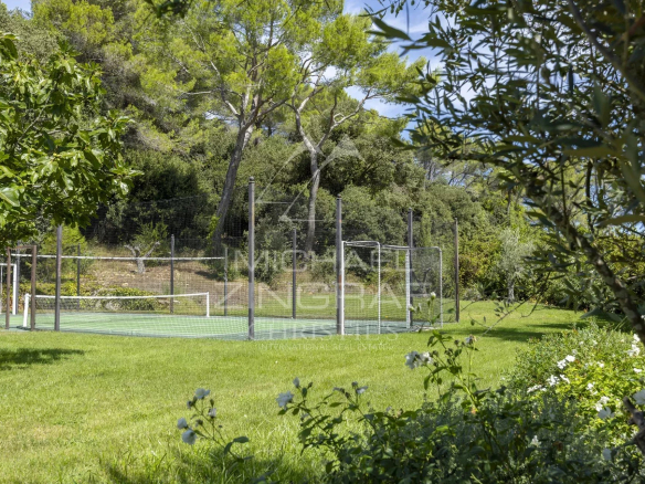 Terrains de tennis dans un jardin verdoyant à Mougins, entouré d'arbres et de fleurs.