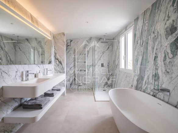 Salle de bain moderne avec baignoire et douche, murs en marbre, fenêtres laissant entrer la lumière.
