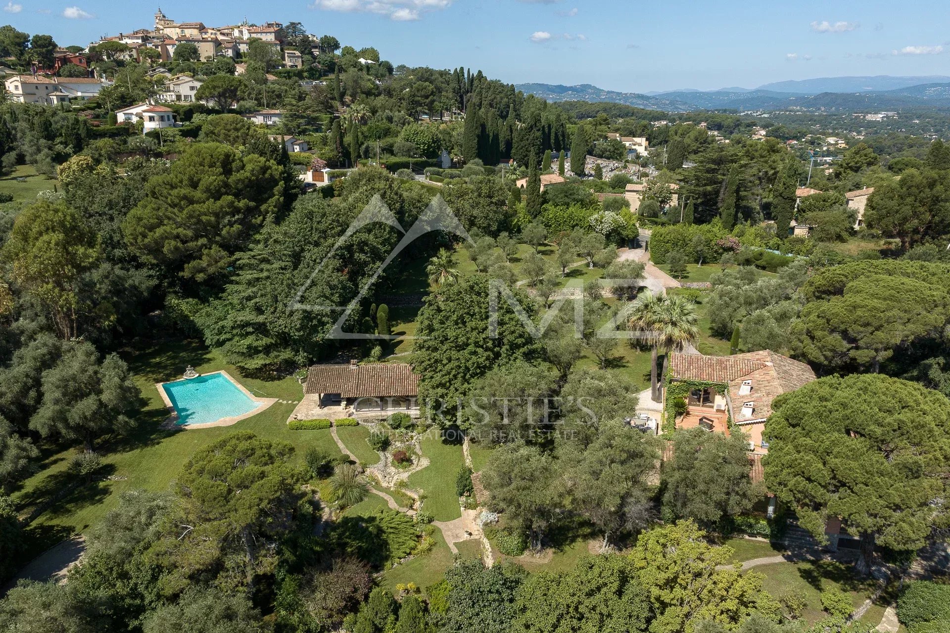 Vue aérienne d'une propriété avec piscine et parc paysager à Mougins, entourée d'arbres et d'oliviers.